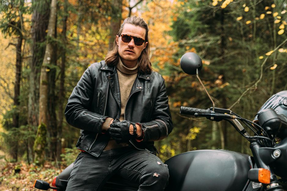 Man in sunglasses and leather jacket on a motorcycle in an autumn forest.