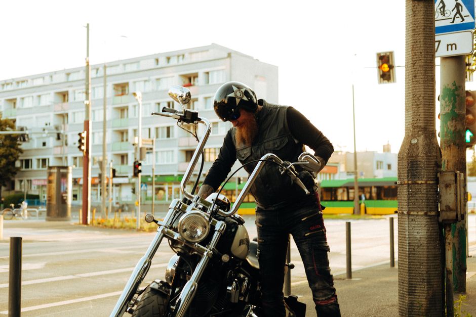 A bearded biker standing with a Harley-Davidson on a city street in Poznań, Poland.