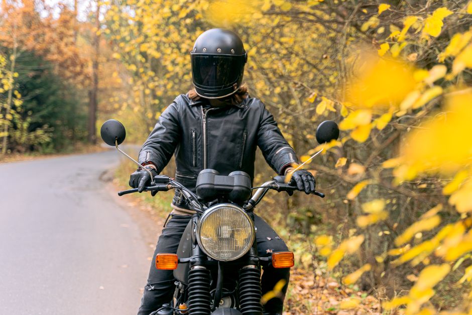 Biker on a motorcycle in a black jacket and helmet rides through a scenic autumn forest road.