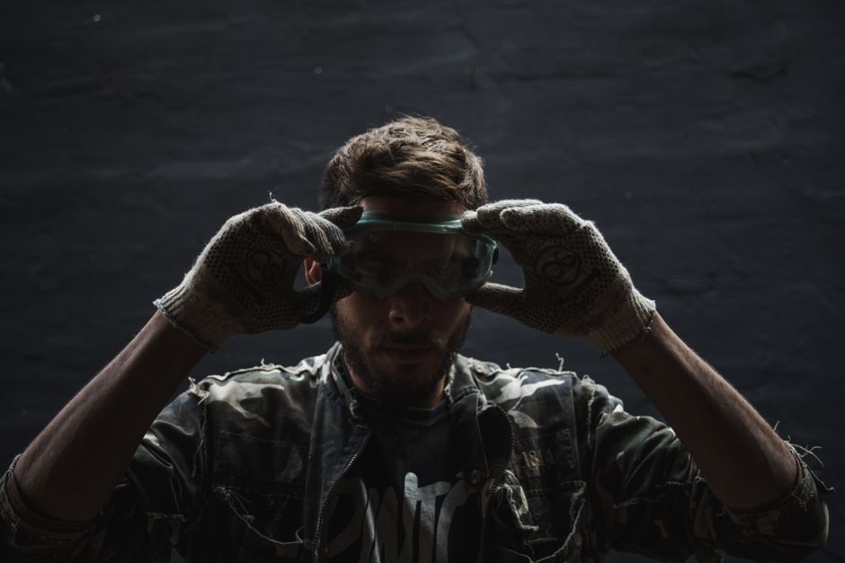 A man adjusting his safety goggles with protective gloves, ensuring safety.